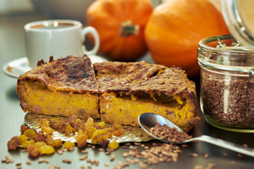 Homemade pumpkin pie with raisins, linseeds and flax flour on wooden table with cup of coffee and pumpkins on the background, copy space, close-up, healthy vegetarian food concept