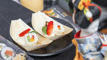 Stand with selection of fast food. Asian street food market. Salmon sushi and sweet style sushi, rice, strawberry, mango, kiwi, chocolate, coconut and mint.