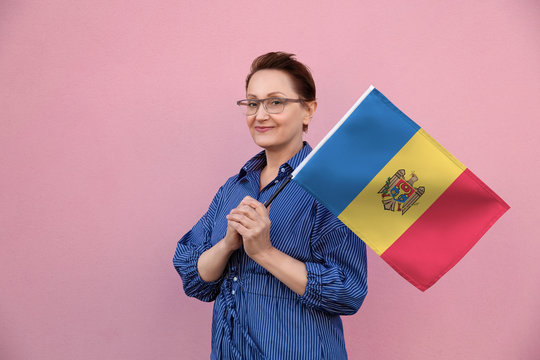 Moldova flag. Woman holding Moldovan flag. Nice portrait of middle aged lady 40 50 years old holding a large flag over pink wall background on the street outdoor.