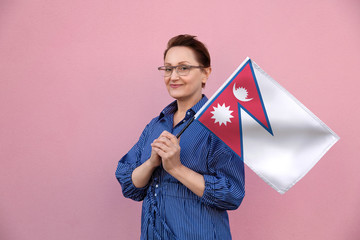 Nepal flag. Woman holding Nepalese flag. Nice portrait of middle aged lady 40 50 years old holding a large flag over pink wall background on the street outdoor.