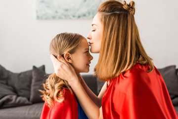 Beautiful mother kissing cute daughter at home
