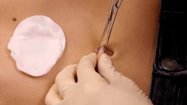 slow motion close view physician uses clamps to hold and stabilize navel tissue on client belly for piercing