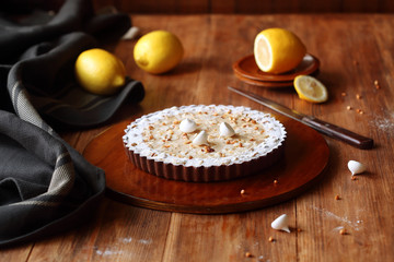 Chocolate Lemon Tart with hazelnuts and meringue cookies, on brown plate, on wooden table.