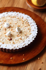 Chocolate Lemon Tart with hazelnuts and meringue cookies, on brown plate, on wooden table.