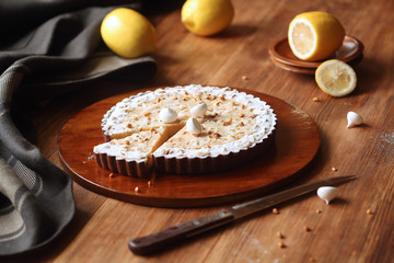 Chocolate Lemon Tart with hazelnuts and meringue cookies, on brown plate, on wooden table.