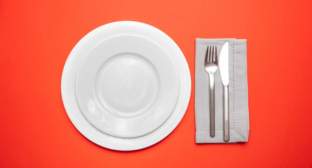 Set of empty white plates and cutlery on red, orange color background