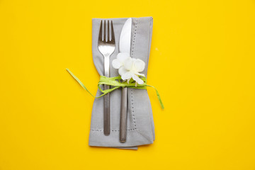 Table place setting in bright yellow. Gray linen napkin and cutlery on yellow color background