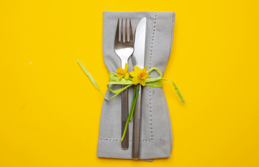 Table place setting in bright yellow. Gray linen napkin and cutlery on yellow color background
