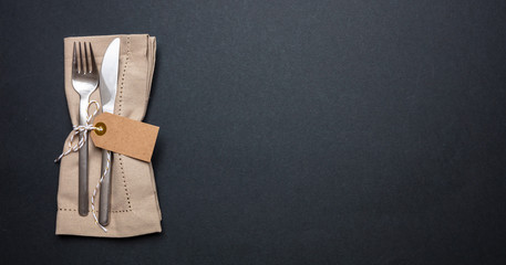 Table place setting with linen napkin and blank tag on black color background, banner