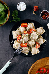 Top view on cut ravioli on fork. homemade ravioli stuffed with herbs, cherry tomato, parmesan, and served on plate on dark concrete background. food menu, recipe concept. Copy space