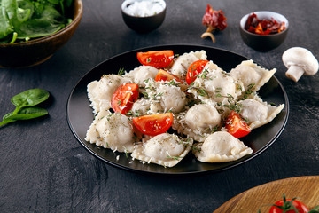 Close up view on Italian homemade ravioli stuffed with herbs, cherry tomato, parmesan, and served on plate on dark concrete background. Restaurant, food menu, recipe concept Lifestyle, copy space.