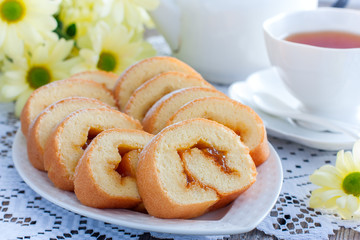 Biscuit roll jam with tea on a white table, horizontal