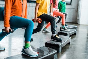 Obraz premium Cropped view of kids with dumbbells training with step platforms