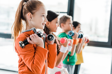 Smiling children in sportswear training with dumbbells