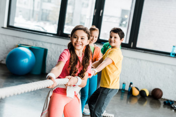 Smiling kids in sportswear pulling rope in gym