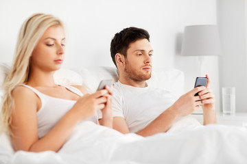 people, technology, internet addiction and communication concept - couple with smartphones in bed