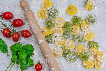 Homemade fresh Italian ravioli pasta on white wood table  with flour, basil, tomatoes,background,top view.
