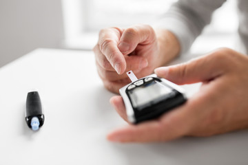 medicine, age, diabetes, health care and old people concept - senior man with glucometer checking...