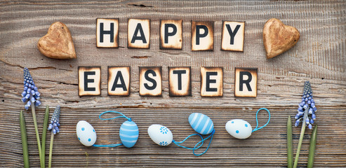 Happy Easter text on rustic wood with blue hyacinth flowers, hearts and Easter eggs