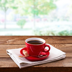 Red cup of tasty coffee on napkin, on wooden table. Spring background