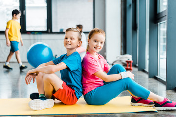 Adorable kids sitting back to back on fitness mat