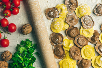 Homemade fresh Italian ravioli pasta on white wood table  with flour, basil, tomatoes,background,top view.