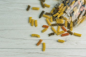 Raw uncooked three-colored Fusilli  on white wood table.
