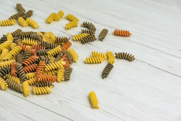 Raw uncooked three-colored Fusilli  on white wood table.
