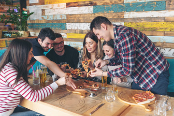 Happy young friends having fun sharing pizza at restaurant 