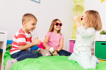 summer, valentines day and childhood concept - happy little kids in heart shaped sunglasses playing at home