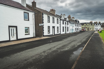 Narrow street in the small town. Northern Ireland. Amazing city scape the cottages in traditional Irish style. Grey cloudy sky before the rain. Attractive tourist destination.