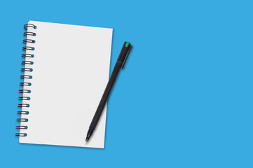 One paper notepad with spiral binder and blank sheets near black plastic pen lies of blue office table. Top view. Copy space for your text. Concept of business or education