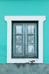 A window of a bright aquamarine, turquoise color house with an old wooden frame and a white paint around it