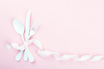 Festive table setting with fork, knife and hearts on pink pastel background.Romantic dinner. Space for text. Top view.