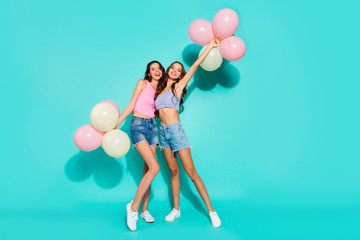 Fototapeta premium Full length body size photo funny beautiful amazing two she her ladies colored balloons hands arms mood beach party wearing shiny jeans denim shorts tank tops isolated teal bright vivid background