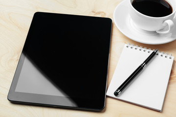 Digital tablet computer and cup of coffee on wooden desk.