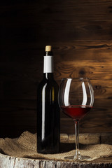 Bottle and glass of red wine on wooden barrel shot with dark wooden background