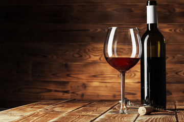 Glass and bottle with delicious red wine on table against wooden background