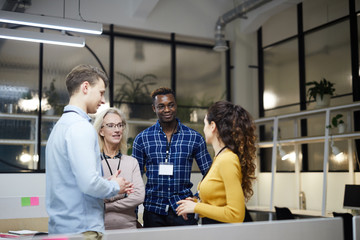 Content multi-ethnic business team in casual clothing standing in circle and discussing presentation while preparing for conference together