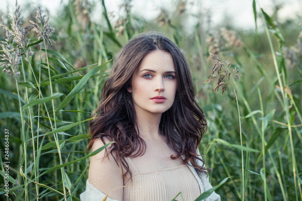 Wall mural beautiful woman outdoors on green grass background in spring romantic cloudy day