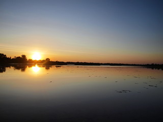 Obraz premium Beautiful sunset over the reservoir and Silhouettes landscape view sunset Water reflection On the background is a black cloud and blue sky.