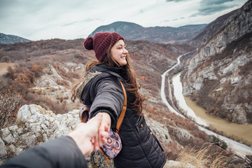 Naklejka premium Back view of young woman with long hair outdoors holding boyfriend's hand on the edge of canyon.