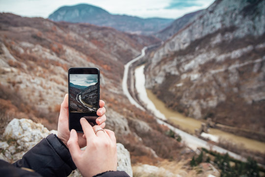 Tourist takes a picture of canyon, river and highway with his smartphone