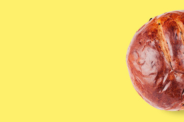 Fototapeta premium One baked circle sugary brown bread with raisins on yellow table in kitchen with copy space for your text. Flat lay