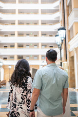 Couple embracing in front of new big modern house, outdoor rear view back looking at their dream home