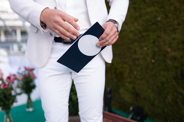 Man shownam in a white suite and red tie holding a plain business card close up