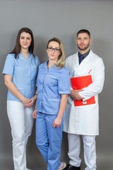 Male doctor and two female nurses on grey background, isolated, concept