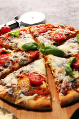 Vegetarian Italian pizza with melted cheese, red tomatoes and green basil on a table decorated by cheese, tomato and cherry tomatoes