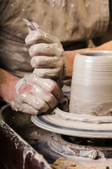 the process of creating a pottery on a twisted Potter's wheel close-up. Dirty hands in the clay and the potter's wheel with the workpiece.