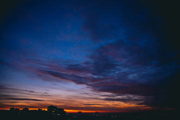 Cityscape with vivid warm dawn. Amazing dramatic blue violet cloudy sky above dark silhouettes of...